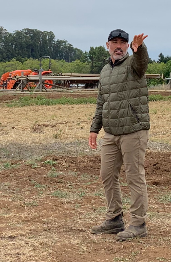 Man standing in a plowed field lecturing about farming